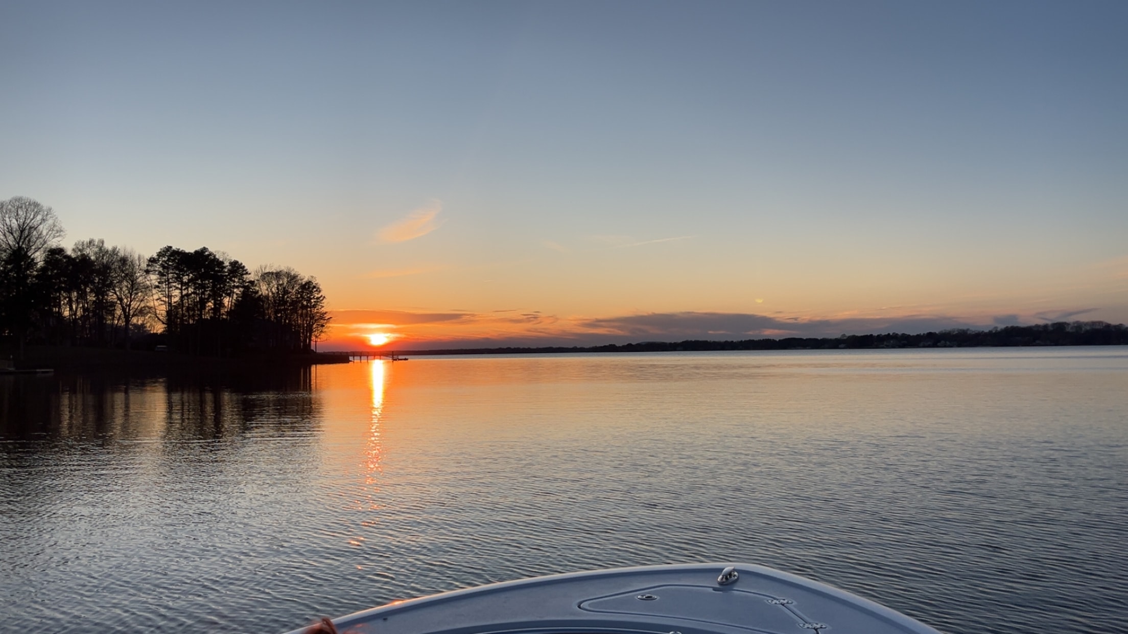Sunrise reflecting off calm Lake Norman water with tree silhouette